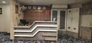 Un área de recepción con un letrero de check-in/out, relojes, un ordenador de escritorio y una fuente de agua.