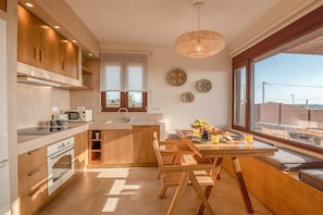 A modern kitchen with wooden cabinets, a built-in oven, and a dining area with a wooden table and chairs. - Sia Elafonisi Pool House (Chrysoskalitissa, Kreta)