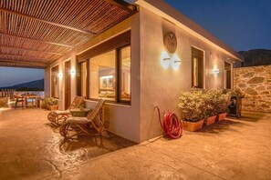 A modern building with large windows, a covered patio area with outdoor furniture, and a stone wall. - Sia Elafonisi Pool House (Chrysoskalitissa, Kreta)