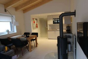 A modern living room with a dining area, a kitchen with a built-in oven, and a black wood-burning stove. - Holiday apartment with 2 bedrooms (Crinitzberg)