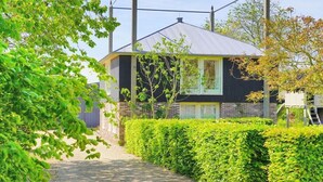 Ett modernt hus med ett tak av metall, omgivet av välskötta häckar och träd.