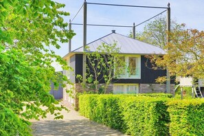 Een modern huis met een metalen dak, omringd door keurig onderhouden heggen en bomen.