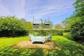 Een terras met een tafel en stoelen, omgeven door een verzorgd gazon en heggen.