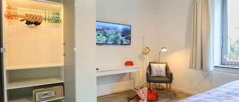 A bedroom with a bed, a TV on the wall, a wardrobe, and a chair with a cushion.