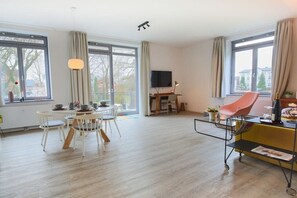 Ein modernes Wohnzimmer mit Essbereich, großen Fenstern, einem Flachbildfernseher und einem gelben Sofa.