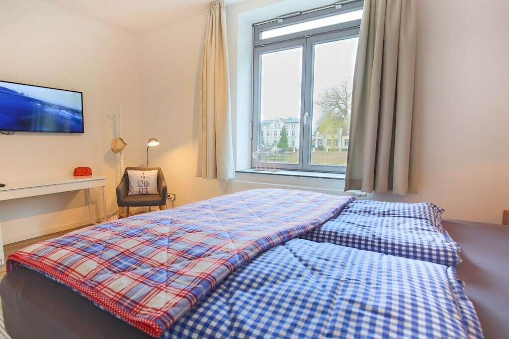 Une chambre à coucher avec un lit, une chaise, un téléviseur et une fenêtre avec des rideaux.