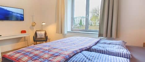 Un dormitorio con una cama, una silla, un televisor y una ventana con cortinas.