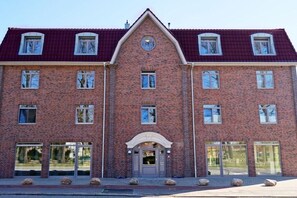 Ein zweistöckiges Backsteingebäude mit einer symmetrischen Fassade, großen Fenstern und einem zentralen Eingang mit dekorativem Bogen.