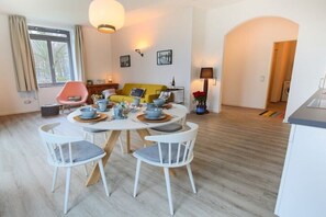 Ein modernes Wohnzimmer mit Essbereich, einer Couch und einer im Hintergrund sichtbaren Küche.