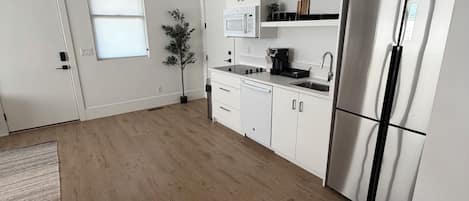 Una cocina moderna con armarios blancos, un refrigerador de acero inoxidable, un microondas y un lavamanos.