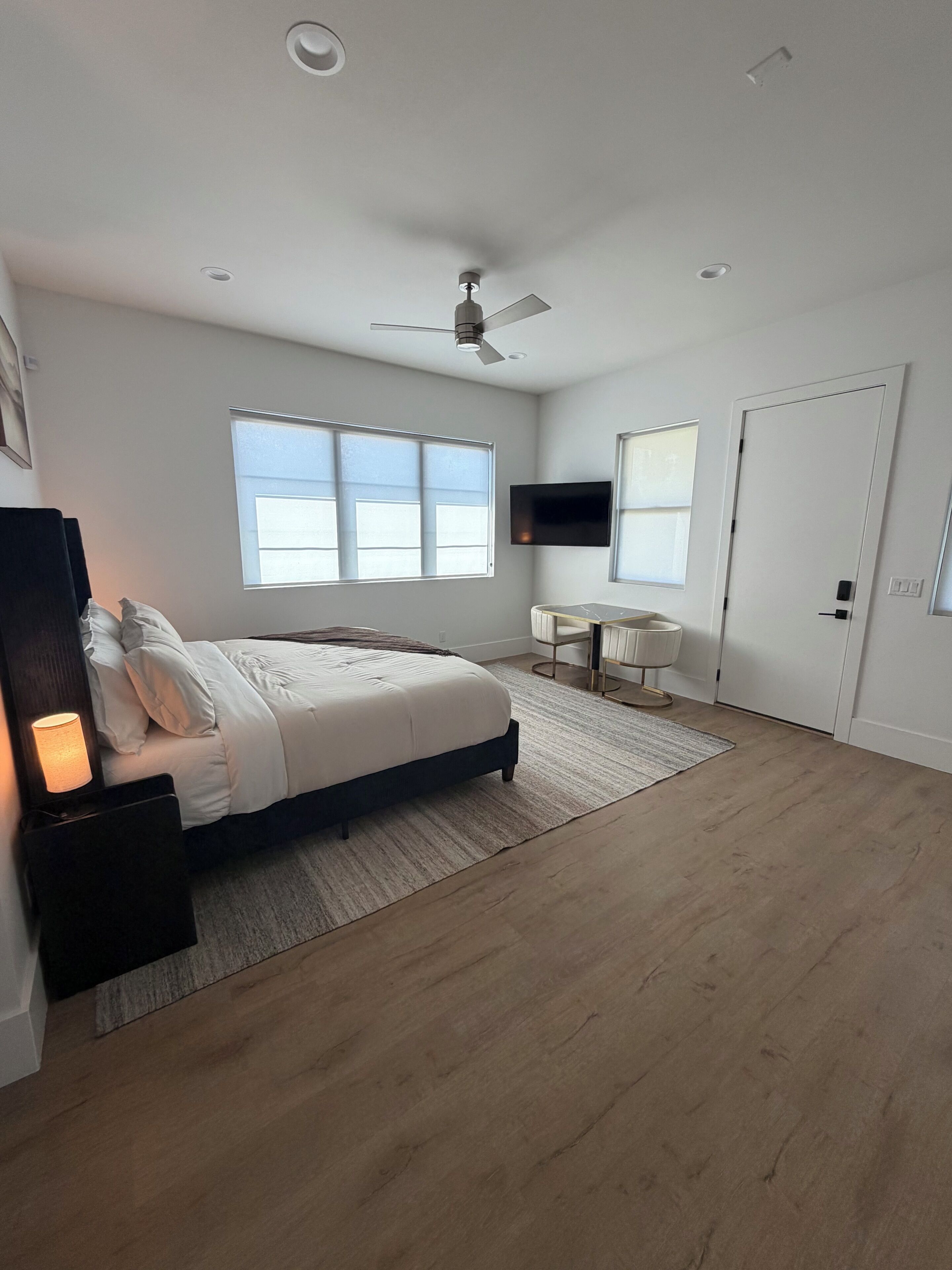 Een moderne slaapkamer met een bed, een bureau, een televisie en een plafondventilator.