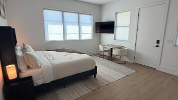 Een moderne slaapkamer met een bed, een bureau, een televisie en een plafondventilator.