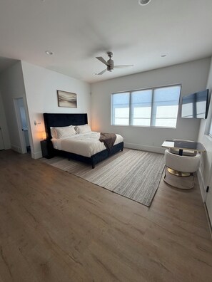 Un dormitorio con cama, ventilador de techo, ventana y mesita de noche.