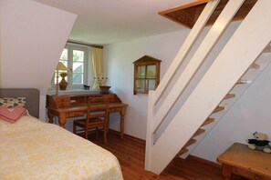 Une chambre à coucher avec un lit, un bureau, une chaise, un escalier en bois et une petite table sur laquelle est posé un ours en peluche.