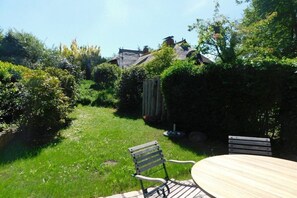 Ein Garten mit einem Holztisch und Stühlen, umgeben von viel Grün und einer Backsteinmauer.