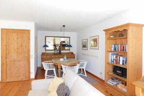 Ein Zimmer mit Holztür, einem Esstisch mit Stühlen, einem weißen Sofa, einem Bücherregal und einem Spiegel an der Wand.