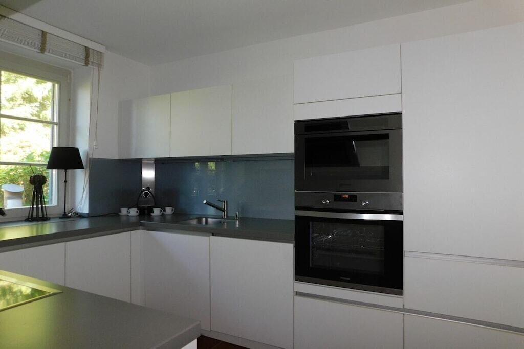 Eine moderne Küche mit weißen Schränken, einem Edelstahlbackofen und einem Fenster mit Blick auf Grünflächen.