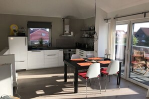 Eine moderne Küche mit weißen Schränken, einer schwarzen Arbeitsplatte und einem Essbereich mit schwarzem Tisch und weißen Stühlen.