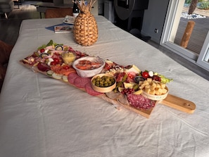 Une table sur laquelle est disposée une planche de charcuterie, avec une variété de viandes, de fromages, d’olives et de fruits.