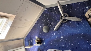 A bedroom with a starry night ceiling, a bed with a patterned bedspread, and a small shelf with decorative items.