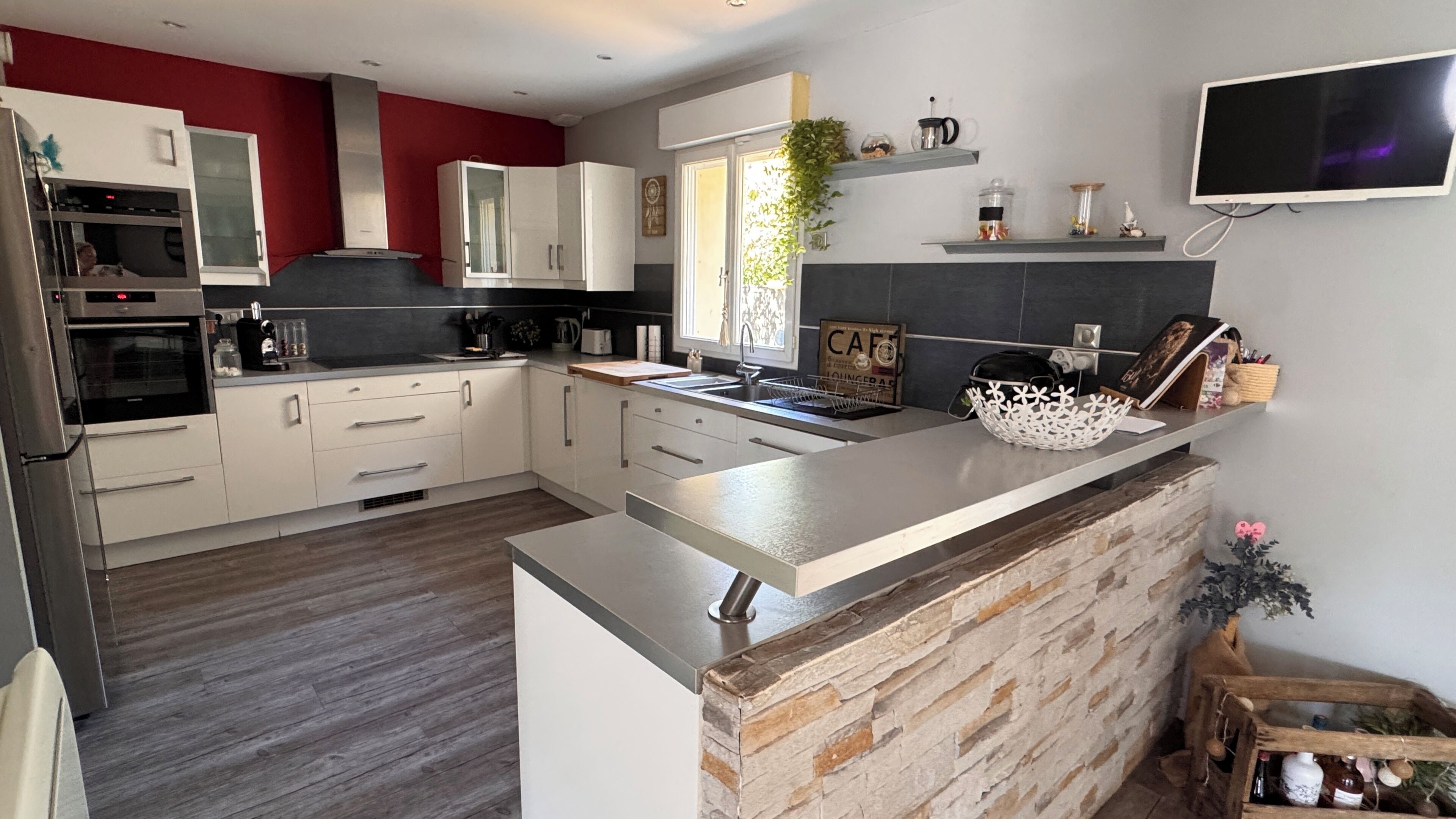 A modern kitchen with a central island, built-in oven, and a flat-screen TV mounted on the wall.