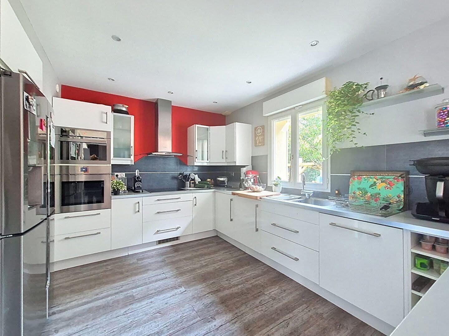 Une cuisine moderne avec des armoires blanches, des appareils en acier inoxydable et un mur d’accent rouge.