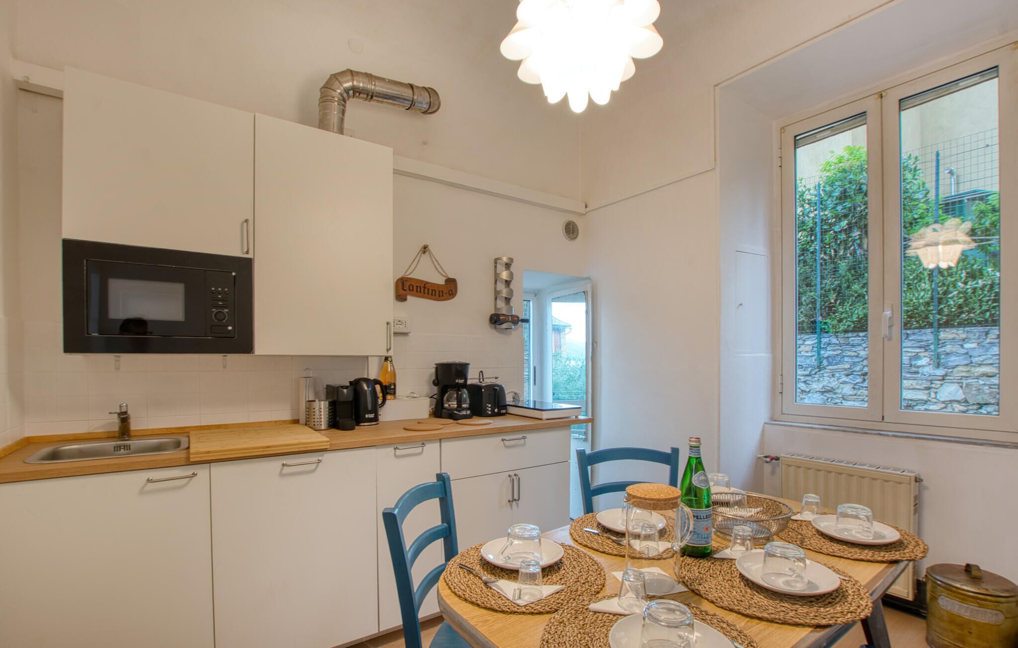 Una cocina con armarios blancos, microondas, cafetera y comedor con mesa dispuesta para cuatro.