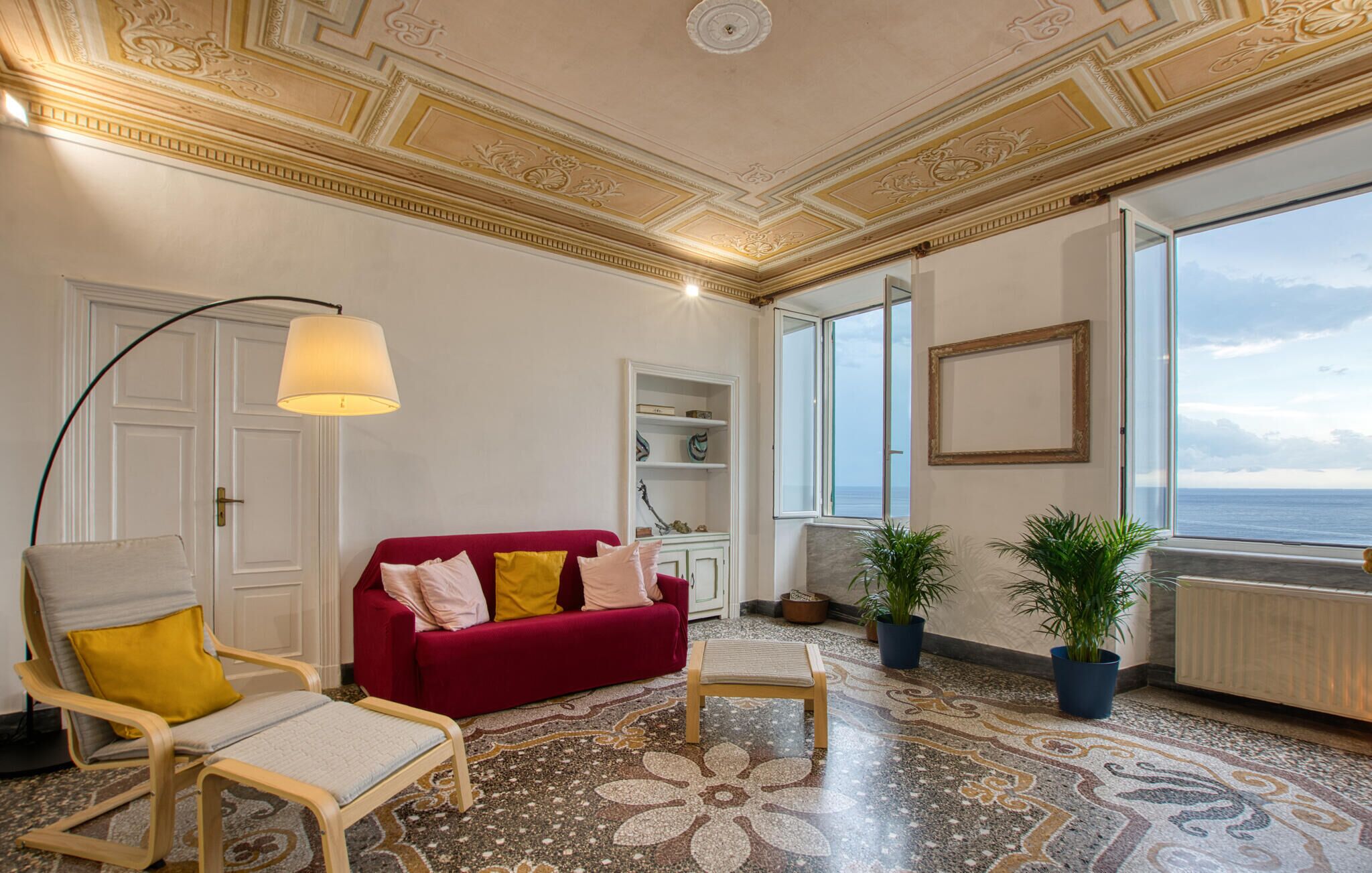 A living room with a red sofa, a wooden chair, a small table, and a floor with a floral pattern.