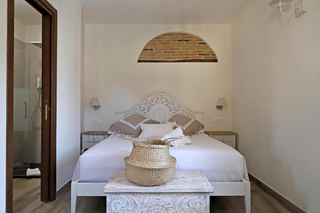 Een slaapkamer met een bed, een nachtkastje, een lamp en een wandplank.