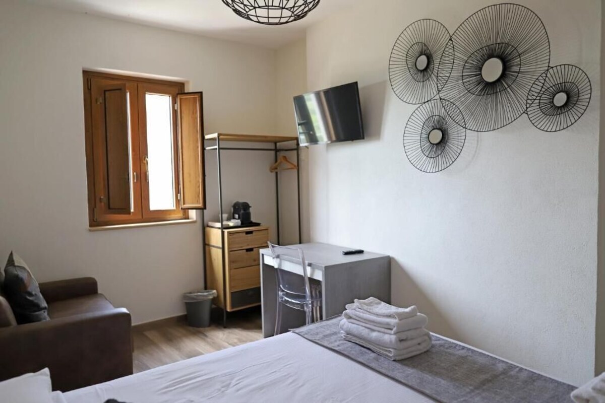 A bedroom with a bed, a desk, a chair, a TV, and a wall art piece.