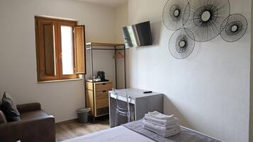 A bedroom with a bed, a desk, a chair, a TV, and a wall art piece.