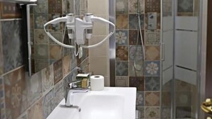 Un baño con un lavabo blanco, un espejo, una ducha con puerta de cristal y baldosas estampadas en las paredes.