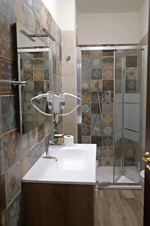 A bathroom with a white sink, a mirror, a shower with a glass door, and patterned tiles on the walls. - CASA MADEO B&B (Macchia Albanese / San Demetrio Corone)
