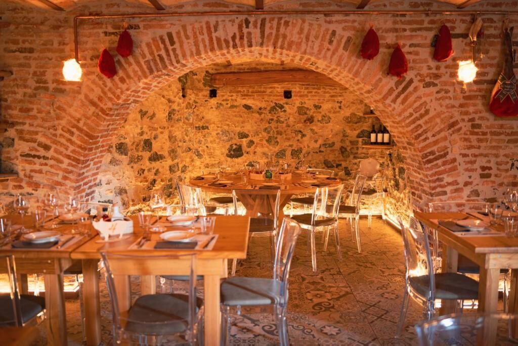 A restaurant with a stone archway, wooden tables, and clear chairs.