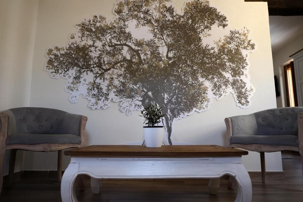 Ein Zimmer mit einer großen Wandmalerei eines Baumes, zwei Sesseln und einem Holztisch.