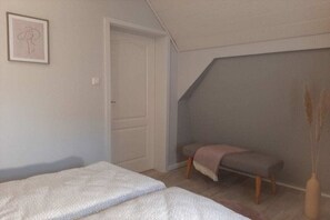 Une chambre à coucher avec un lit, un banc, une porte et un mur orné d’un tableau.