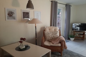 Ein Wohnzimmer mit einer Couch, einem Tisch mit einer Vase, einer Lampe und einem Fernseher.