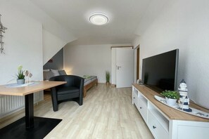Ein modernes Wohnzimmer mit einem Flachbildfernseher, einem Holzessttisch, einem schwarzen Sofa und einer Treppe, die in einen anderen Raum führt.