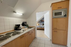 Eine kleine Küche mit Mikrowelle, Herd und Kaffeemaschine. Ein Holzschrank ist zu sehen, und im angrenzenden Raum steht ein Bett.