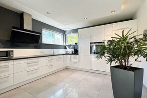 A modern kitchen with white cabinets, a black microwave, and a large potted plant. - Seaside Lounge Rügen (Glowe)