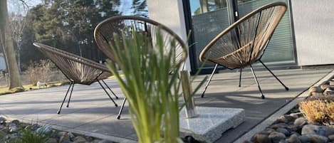 Duas cadeiras de vime em frente a um edifício, com um caminho de pedra e um jardim de pedras.