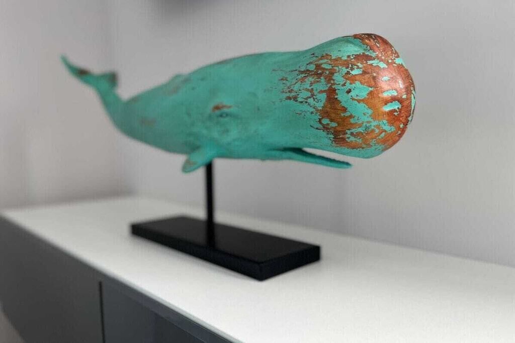 Una escultura de ballena color aguamarina sobre un pedestal negro.