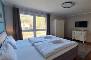 A bedroom with a large bed, a wardrobe, a television, and a window with curtains. - Seaside Lounge Rügen (Glowe)