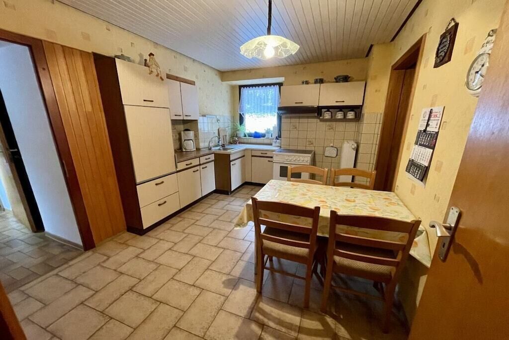 Une cuisine compacte avec un coin repas, des meubles en bois, un pare-feu en carreaux et un luminaire suspendu.
