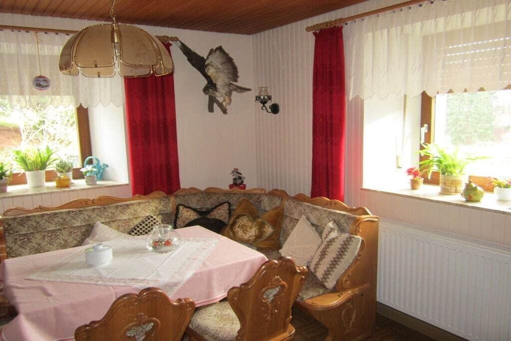 A cozy dining area with a wooden bench and table, red curtains, and a wall-mounted bird decoration.