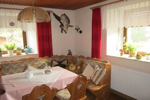 A cozy dining area with a wooden bench and table, red curtains, and a wall-mounted bird decoration. - Holiday apartment with 1 bedroom (Steffeln)