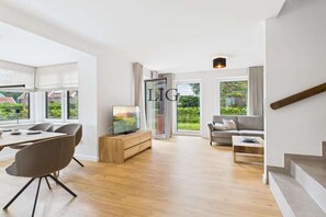 Ein modernes Wohnzimmer mit Essbereich, einer Sofagarnitur und einem Fernseher auf einer Holzeinrichtung.
