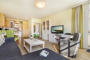 A modern living room with a sofa, a coffee table, and a television. There is a kitchen area with cabinets and a dining table. - 6 in the Granitz house (Binz)