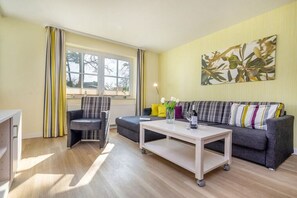 A living room with a sofa, armchairs, a coffee table, and a large window with curtains. - 6 in the Granitz house (Binz)