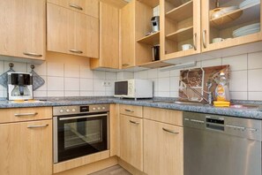 A kitchen with wooden cabinets, a microwave, an oven, and a dishwasher. - 6 in the Granitz house (Binz)